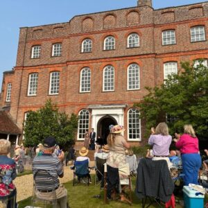 Applauding audience on the back lawn at Finchcocks. Two pianists stand on the outdoor stage next to the Bosendorfer smiling.