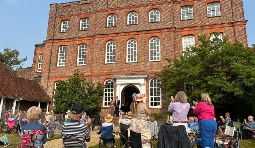 Applauding audience on the back lawn at Finchcocks. Two pianists stand on the outdoor stage next to the Bosendorfer smiling.