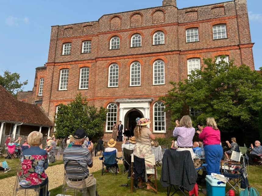 Applauding audience on the back lawn at Finchcocks. Two pianists stand on the outdoor stage next to the Bosendorfer smiling.